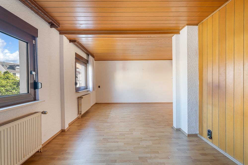 Leerer Raum mit Holzdecke, Holzfußboden, großen Fenstern und weißen Wänden.