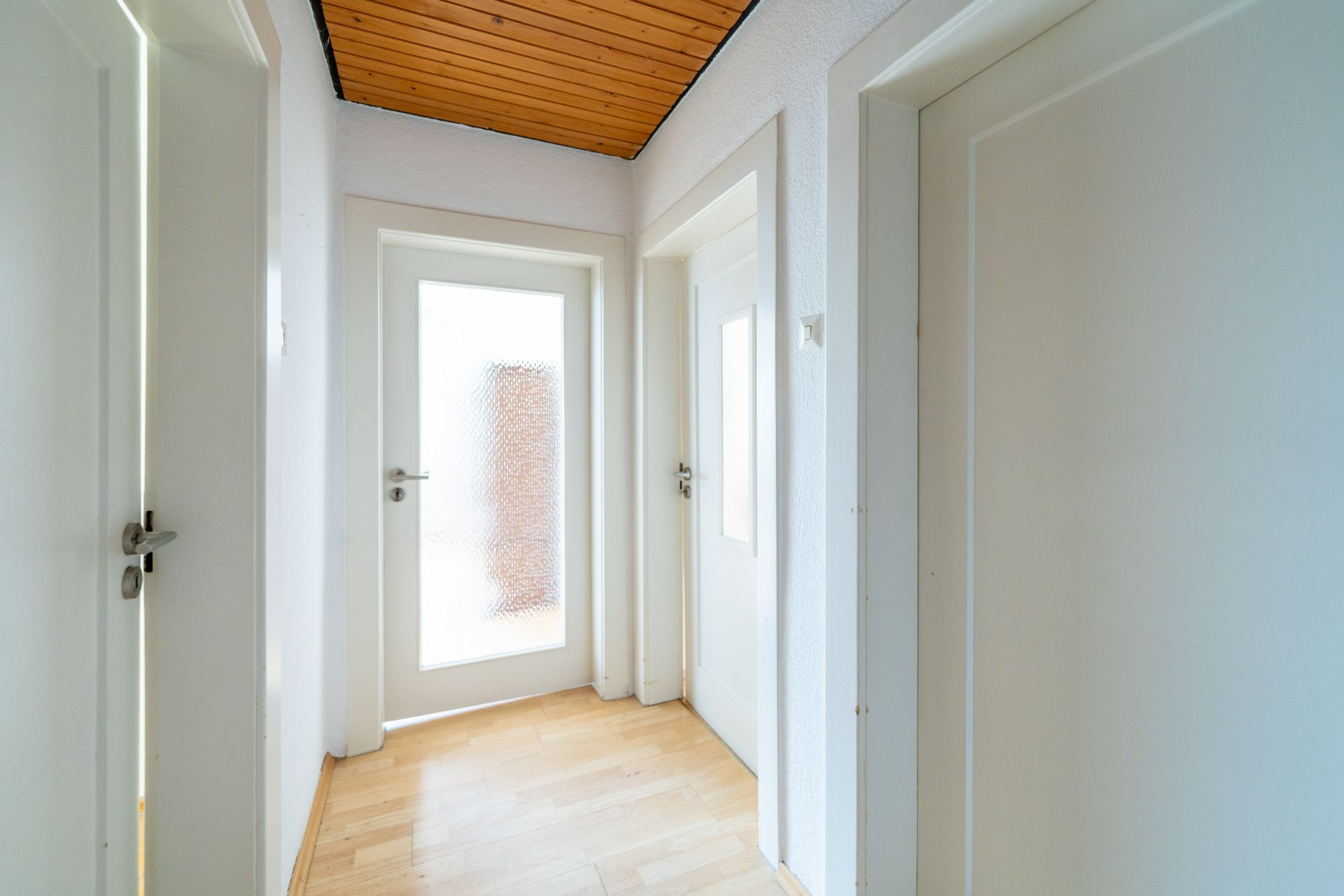 Heller Flur mit Holzboden, weißen Türen und Holzdecke in einer Wohnung.