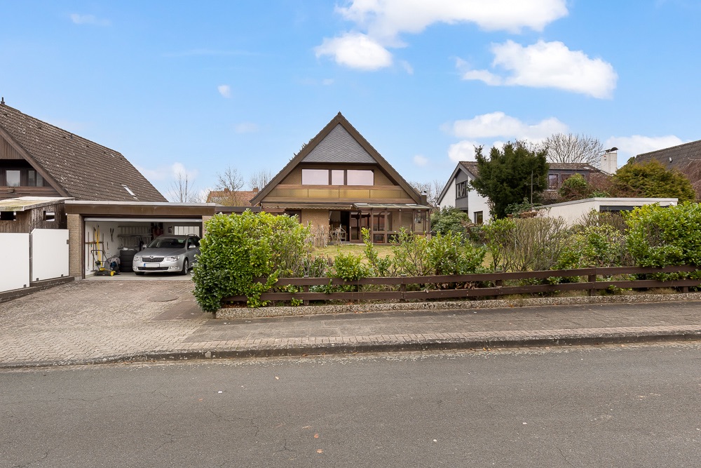 Einfamilienhaus mit spitzem Dach, Gartenzaun und Einfahrt mit geparktem Auto.
