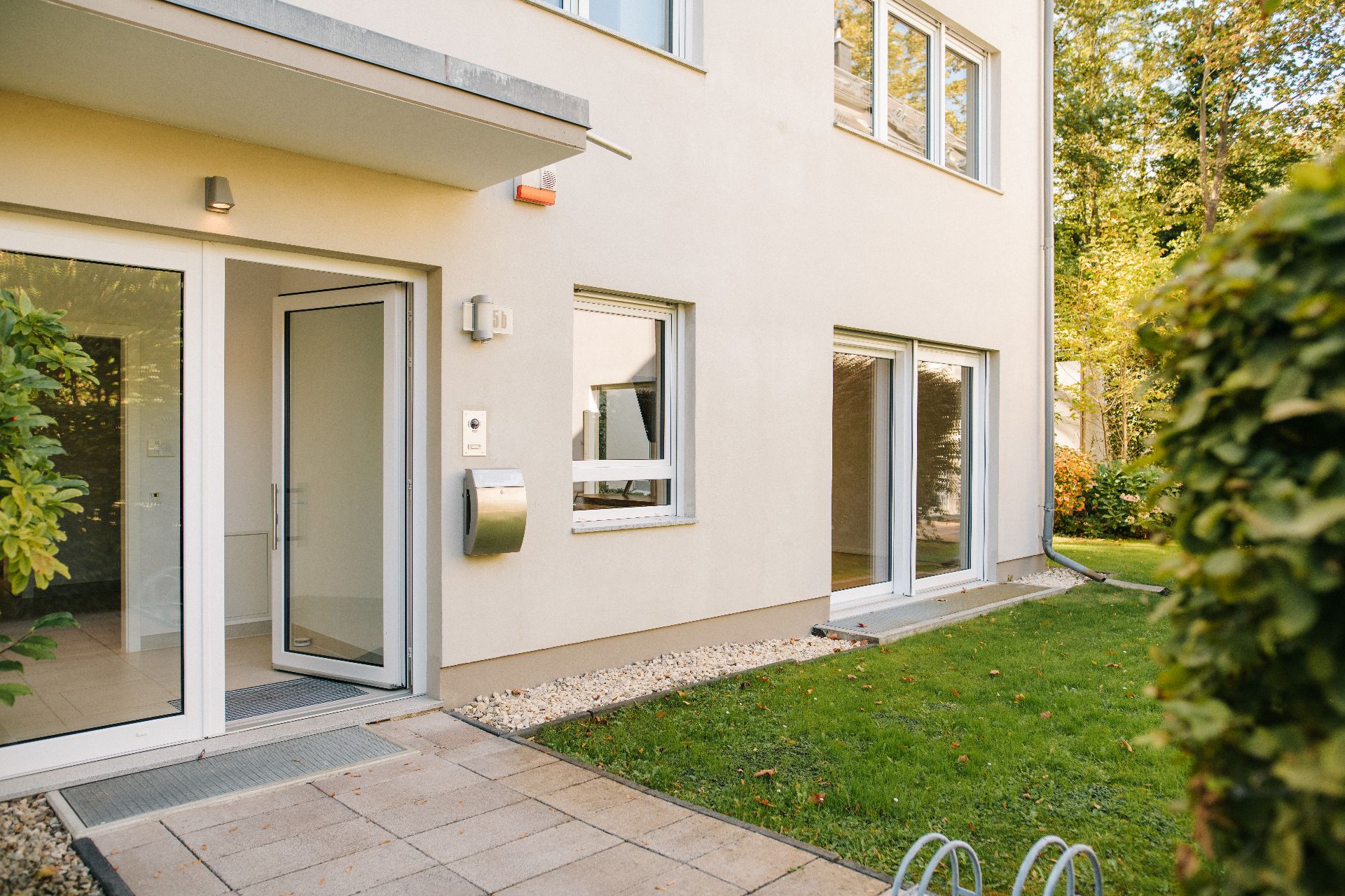 Eingang und Terrasse eines modernen Wohnhauses mit Rasenfläche und großen Fenstern.