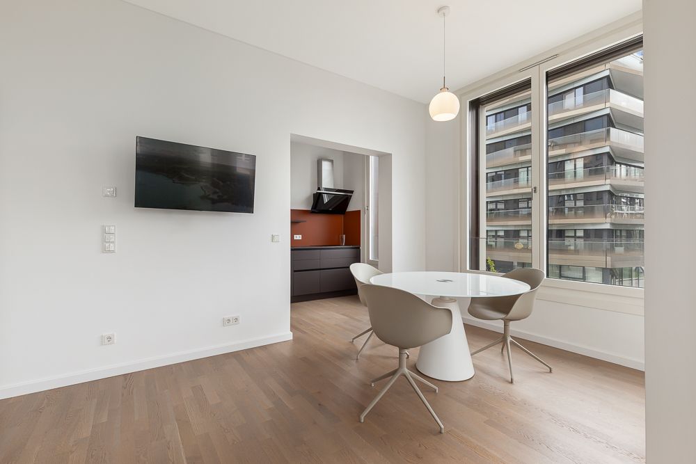 Moderner Essbereich mit rundem Tisch, drei Stühlen, großem Fenster und Blick auf einen Balkon.