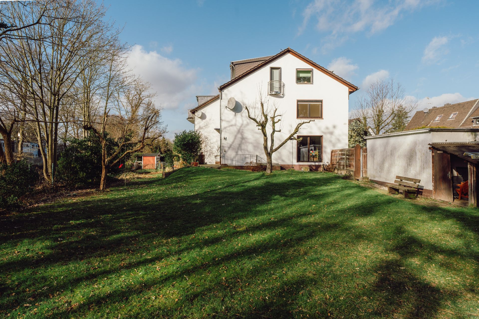 Weißes Wohnhaus mit großem Garten, Bäumen und Schuppen an einem sonnigen Tag.