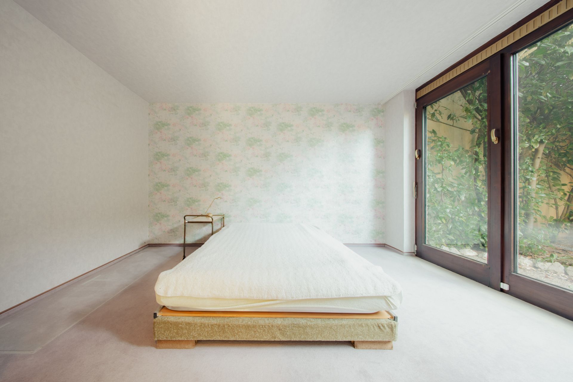 Schlafzimmer mit niedrigem Bett, kleinem Tisch und großen Fenstern mit Blick ins Grüne.