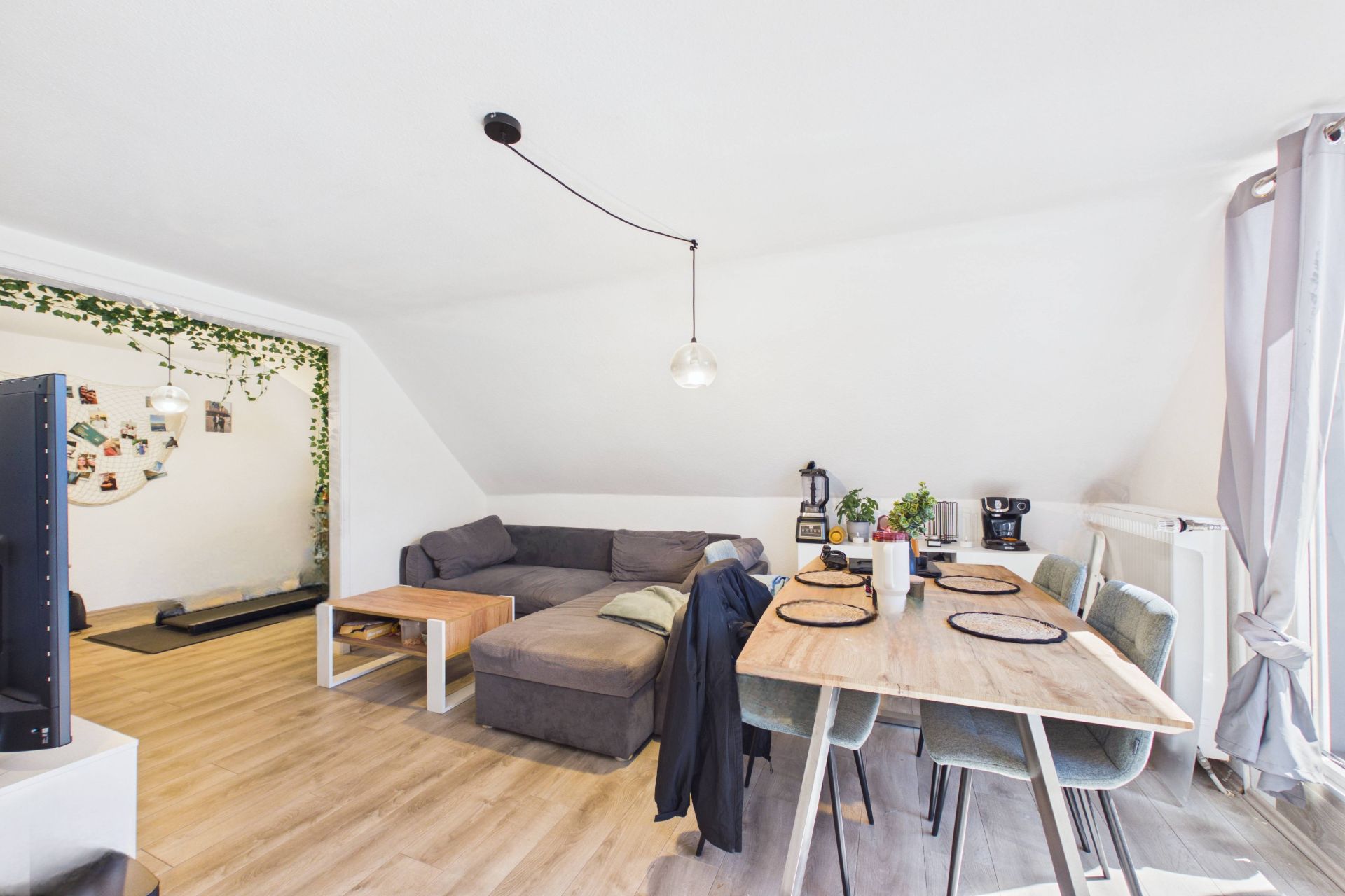 Helles Wohnzimmer mit grauem Ecksofa, Esstisch und Stühlen unter Dachschräge.