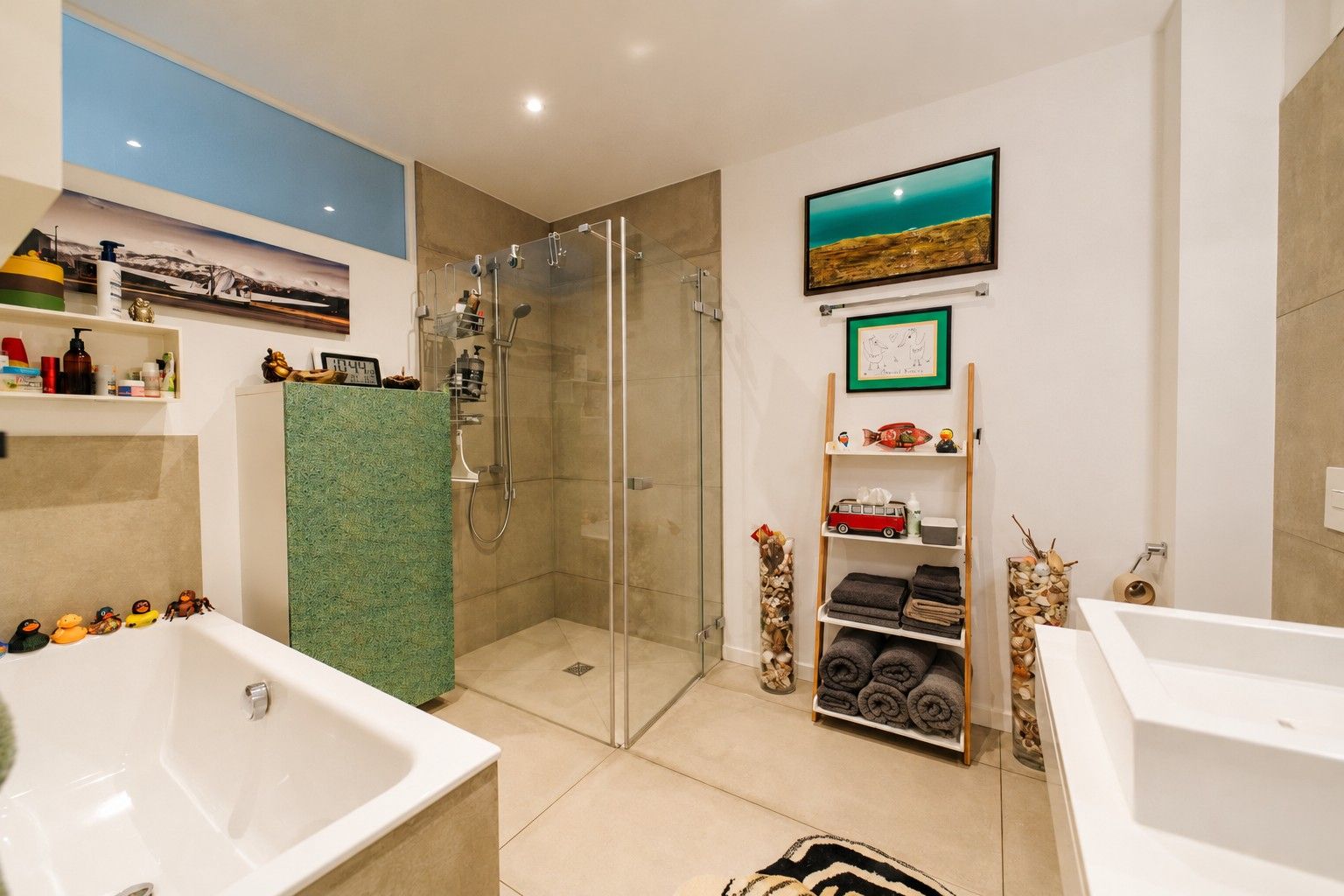 Modernes Badezimmer mit Badewanne, Glasdusche, Regal mit Handtüchern und Dekoration an den Wänden.