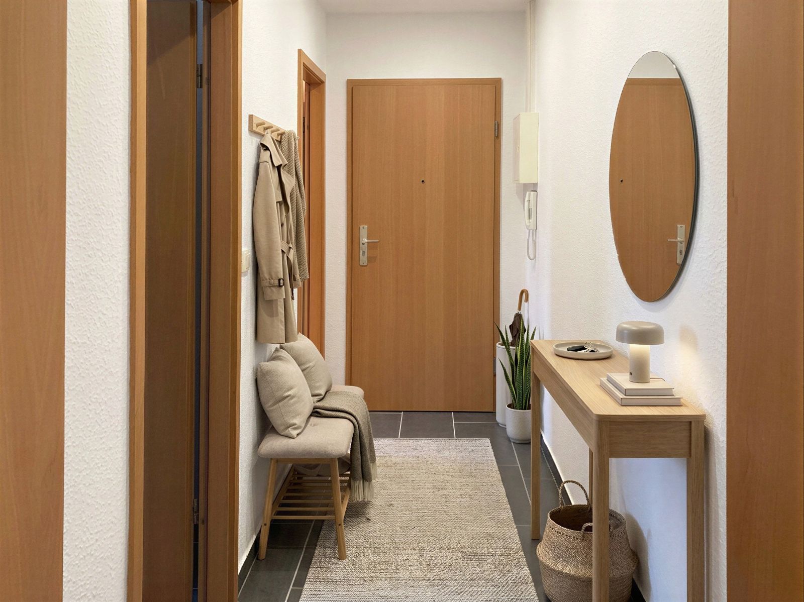 Heller Flur mit Holztür, Spiegel, Sitzbank, Garderobe und schmalem Tisch mit Lampe.
