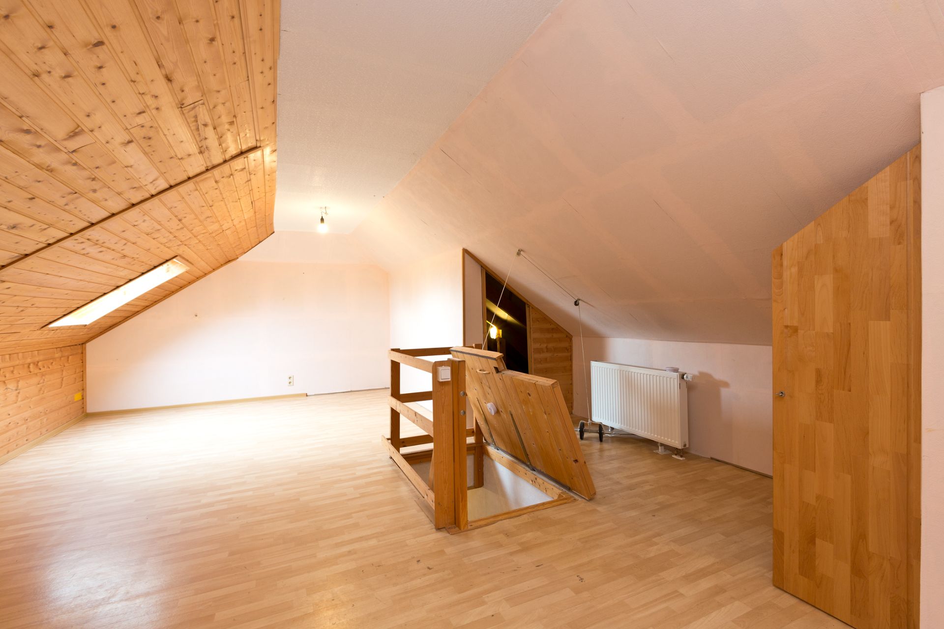 Heller Dachbodenraum mit Holzverkleidung, offenem Treppenabgang und Dachfenster.