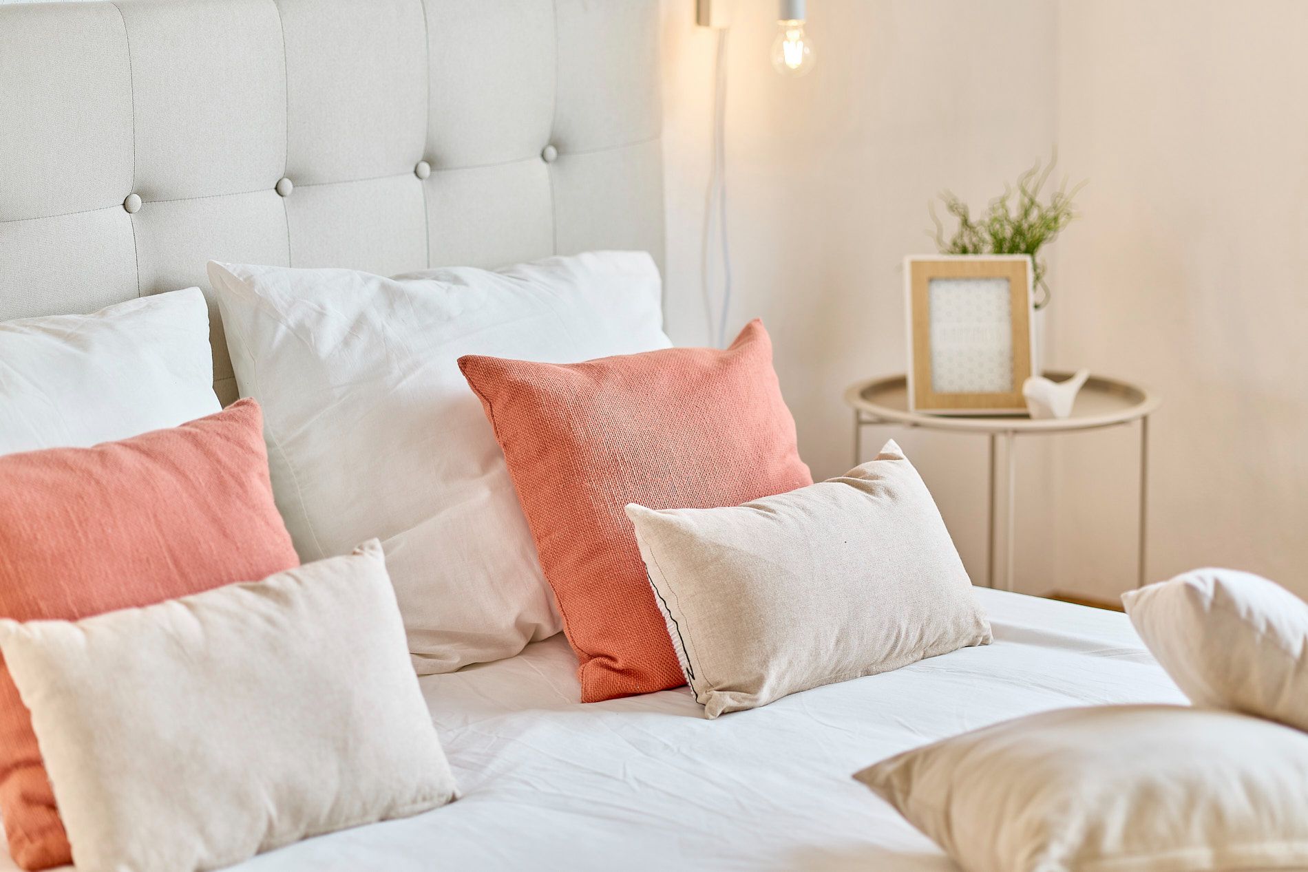 Bett mit weißen und rosa Kissen, Nachttisch mit Pflanze und Bilderrahmen.