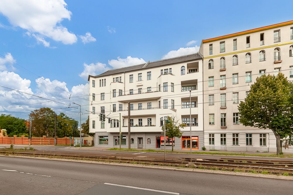 Mehrstöckiges Wohngebäude an einer Straße mit Bäumen und Straßenbahnschienen.