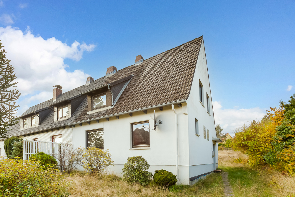 Außenansicht eines weißen Wohnhauses mit Satteldach und Garten bei sonnigem Wetter.