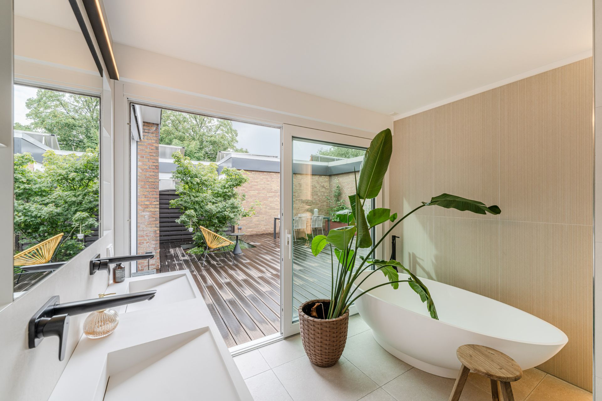 Modernes Badezimmer mit freistehender Badewanne, großer Pflanze und Zugang zu einer Terrasse.