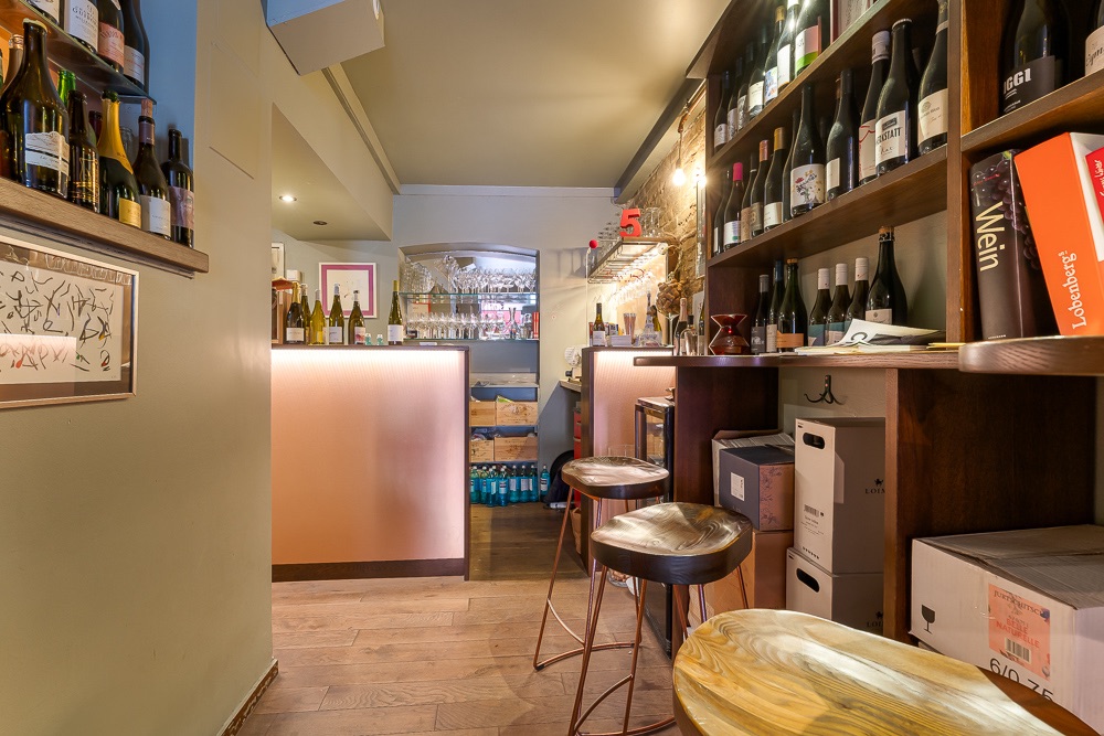 Kleine Hausbar mit Holzstühlen, Regalen voller Weinflaschen und beleuchtetem Tresen.