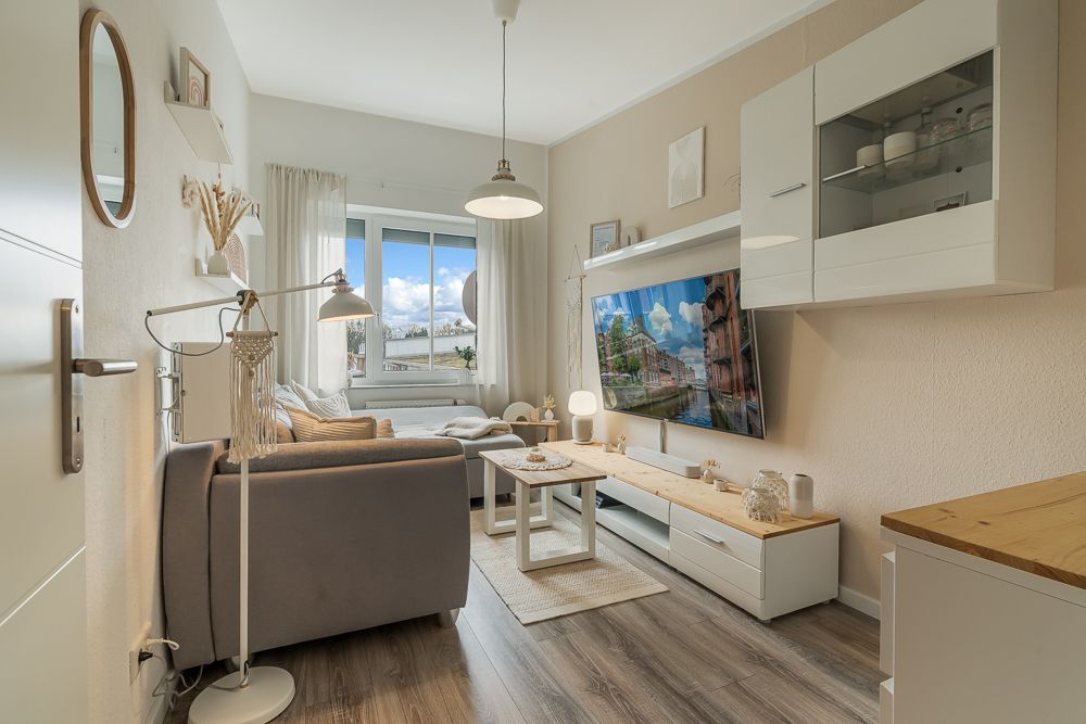Helles Wohnzimmer mit Sofa, Couchtisch, großem Fernseher und Fenster mit Blick nach draußen.