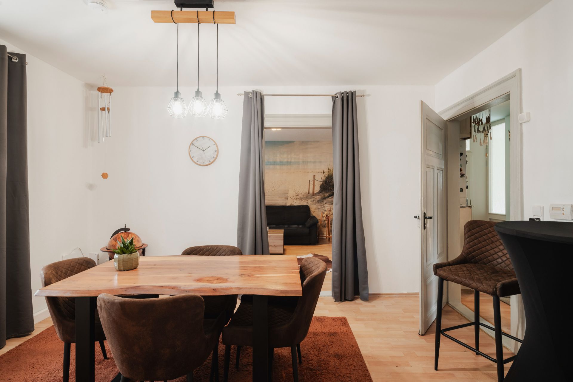 Esszimmer mit Holztisch, sechs Stühlen, Wanduhr und Blick in ein angrenzendes Wohnzimmer.