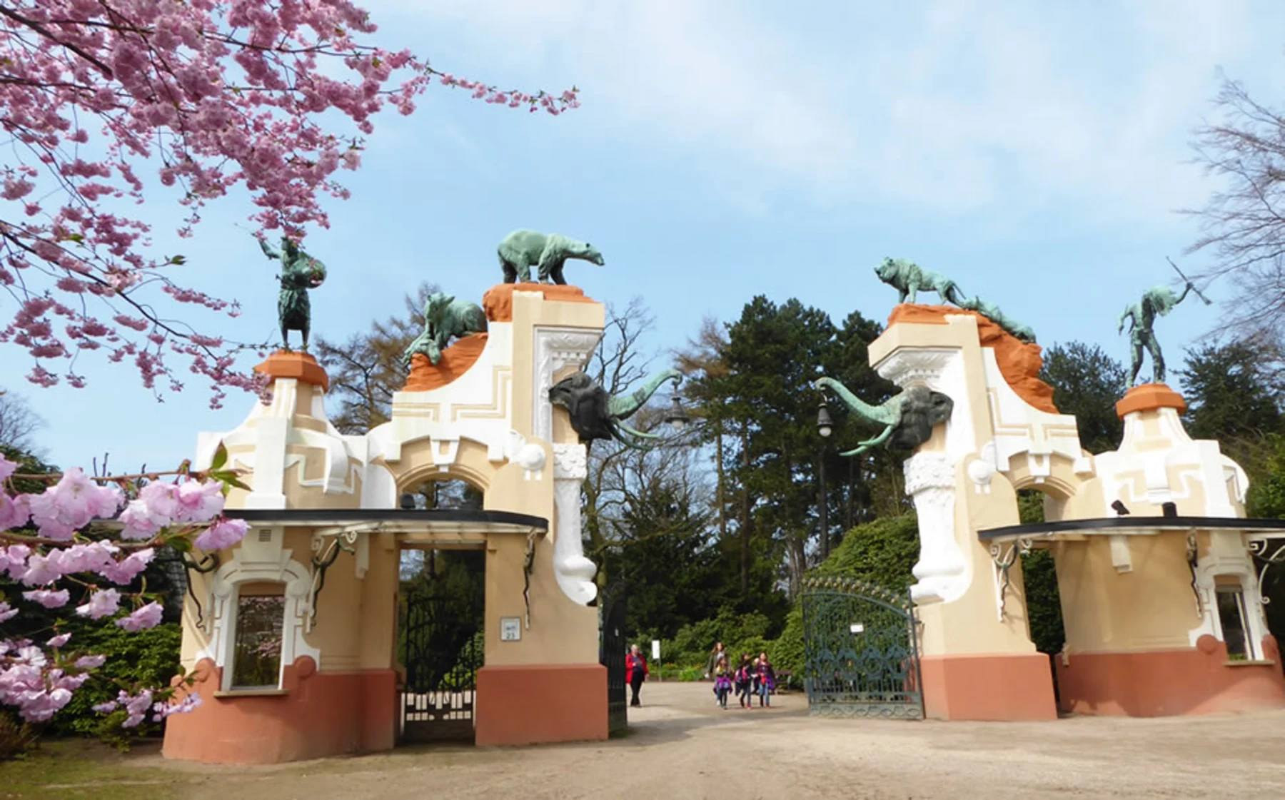Dekoratives Eingangstor mit Tierstatuen und blühenden Kirschbäumen im Vordergrund.