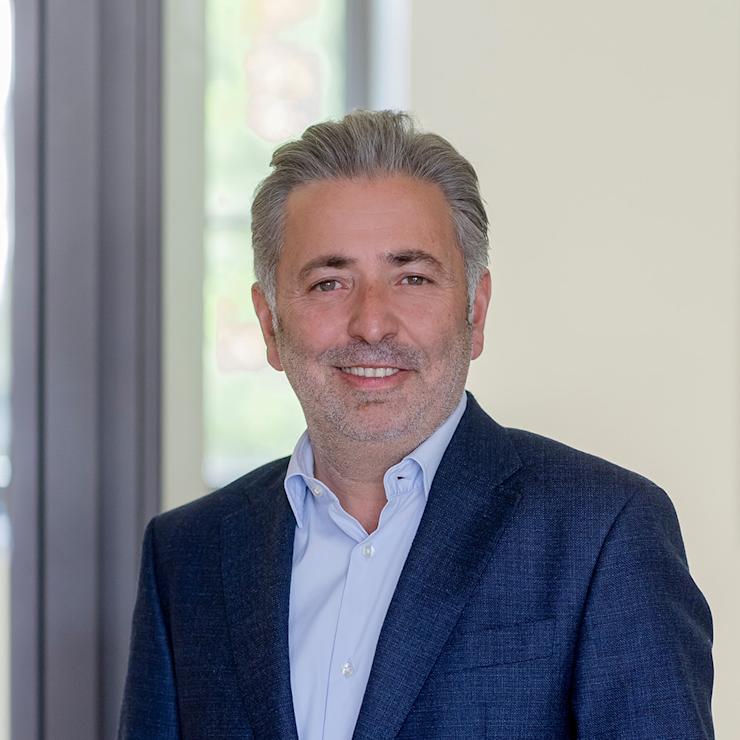 Ein Mann in einem blauen Anzug steht vor einem Fenster und lächelt in die Kamera.