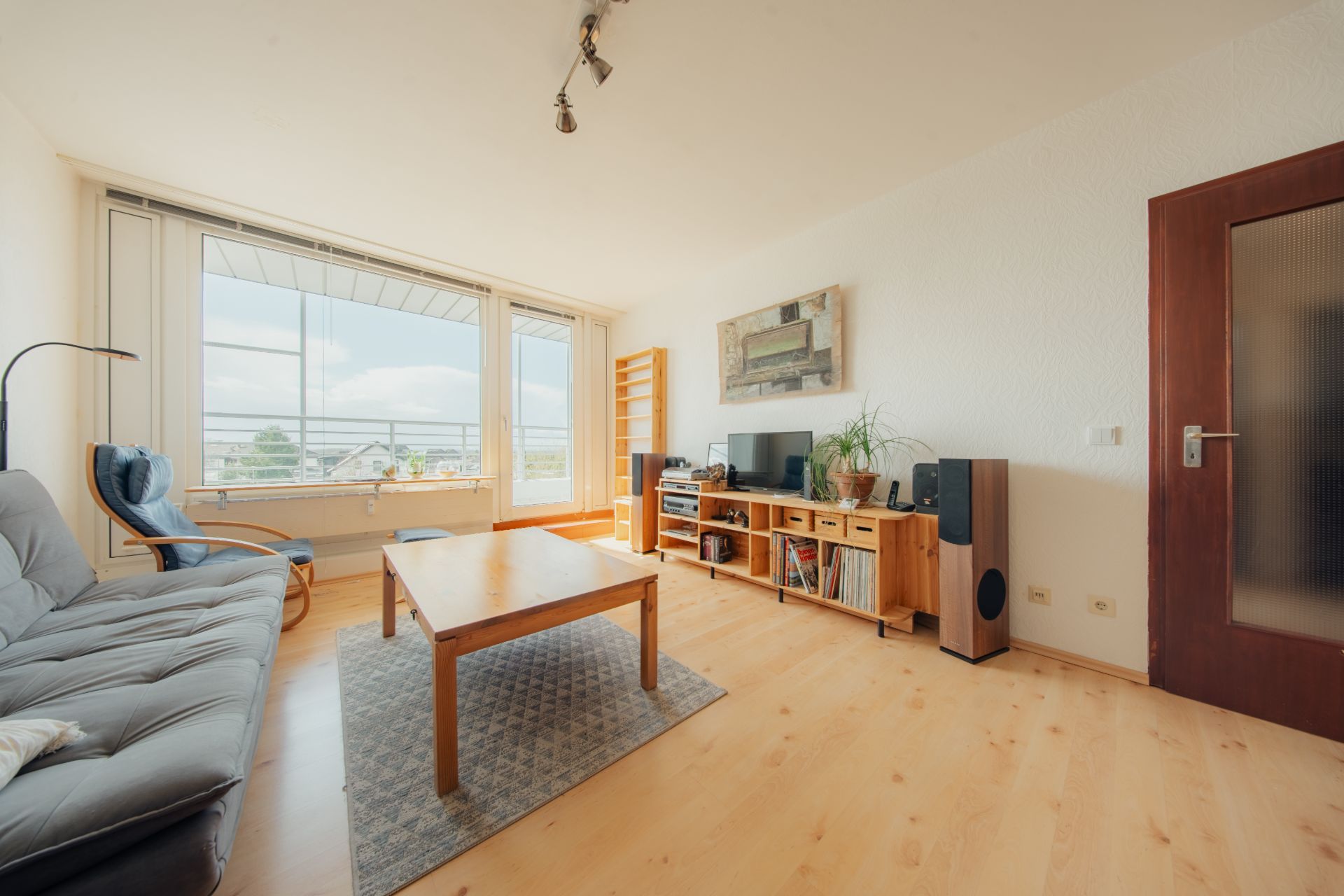 Helles Wohnzimmer mit Sofa, Tisch, Sessel und großem Fenster zur Terrasse.