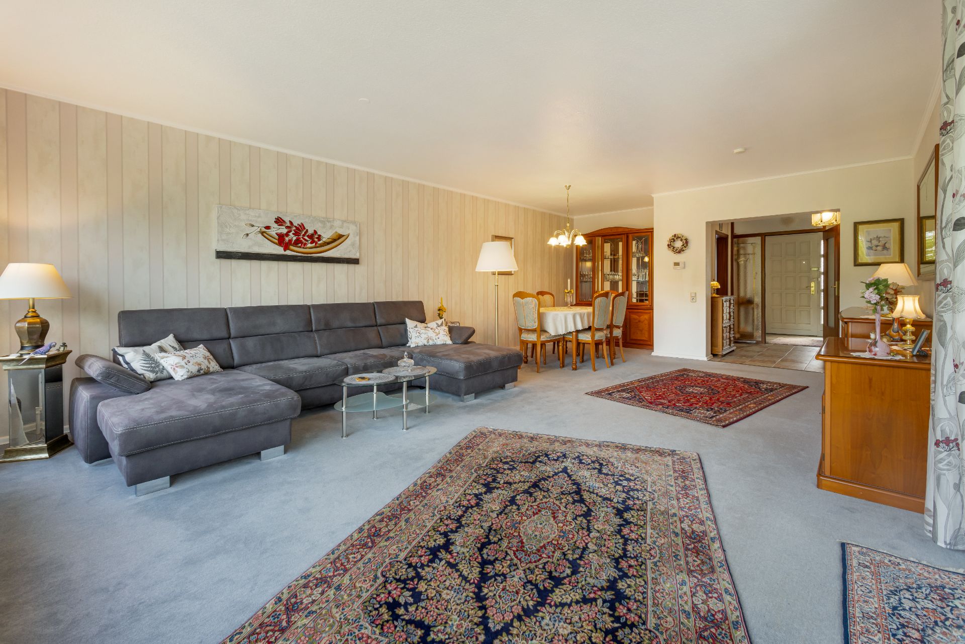 Geräumiges Wohnzimmer mit grauem Sofa, Teppichen, Esstisch und Holzmöbeln.