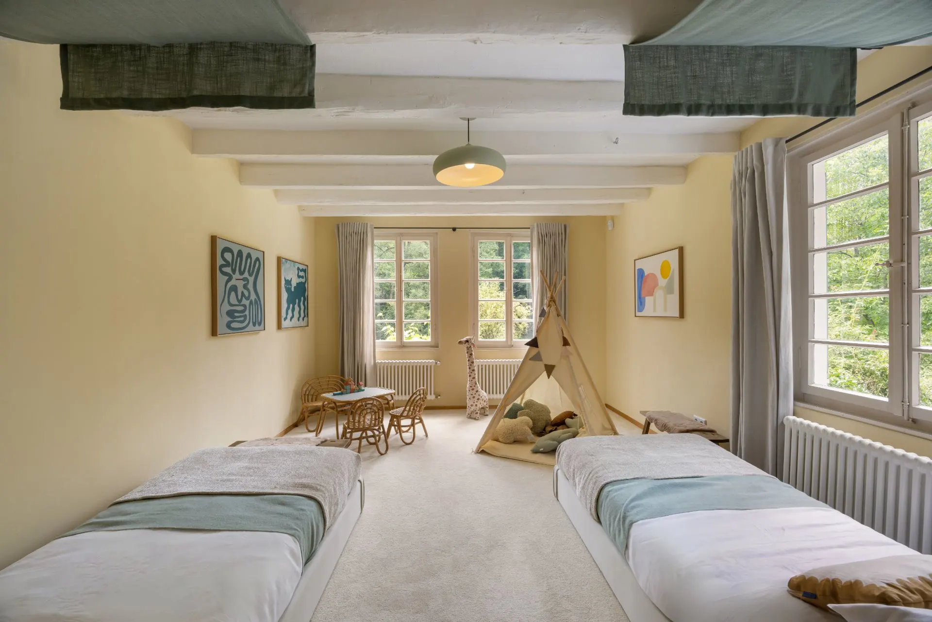 Helles Schlafzimmer mit zwei Einzelbetten, Spielzelt und großen Fenstern mit Blick nach draußen.