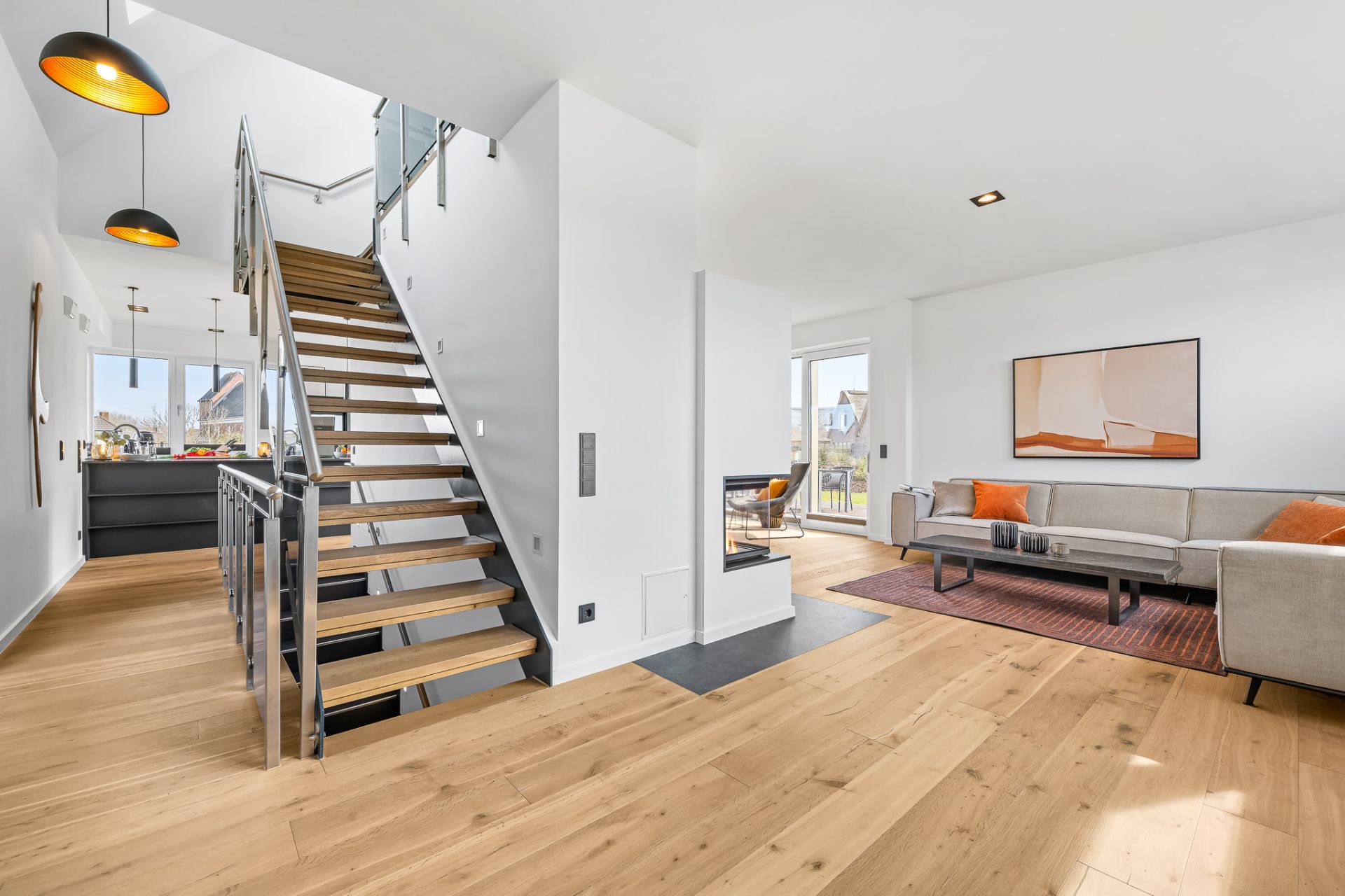Helles Wohnzimmer mit Holzfußboden, Treppe, Sofa, Couchtisch und großem Fenster.