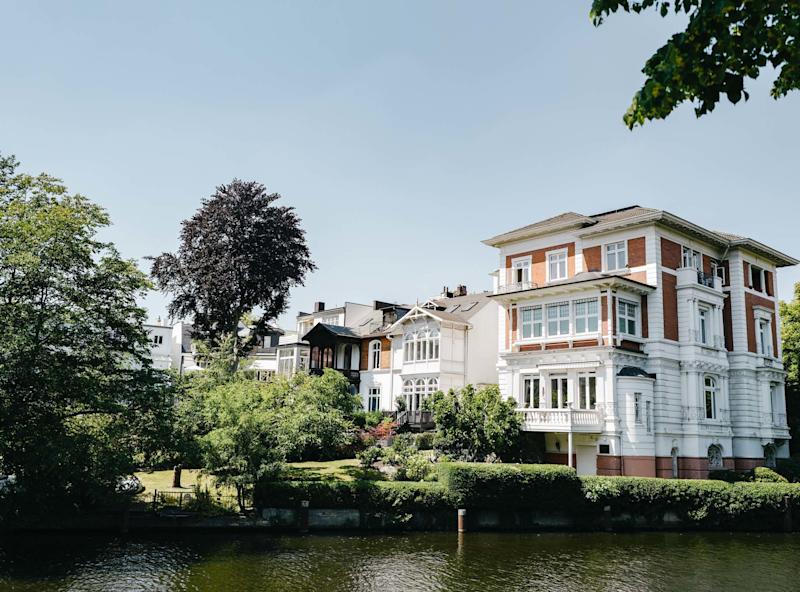 Großes Wohnhaus mit Garten am Wasser, umgeben von Bäumen bei klarem Himmel.