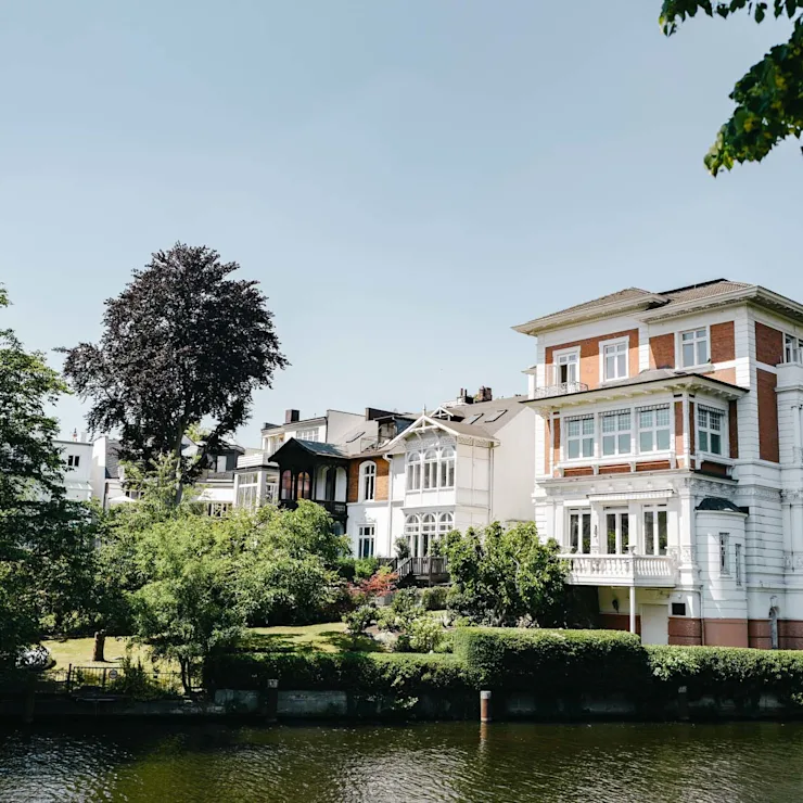 Großes Wohnhaus mit Garten am Wasser, umgeben von Bäumen bei klarem Himmel.