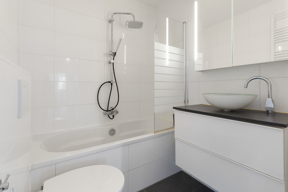 Modernes Badezimmer mit Badewanne, Waschbecken, Spiegel und weiß gefliesten Wänden.