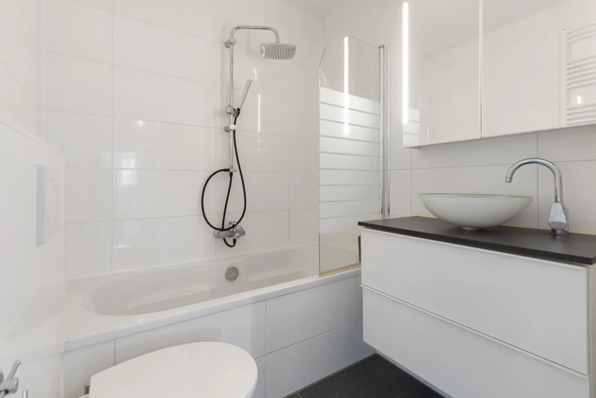 Modernes Badezimmer mit Badewanne, Waschbecken, Spiegel und weiß gefliesten Wänden.
