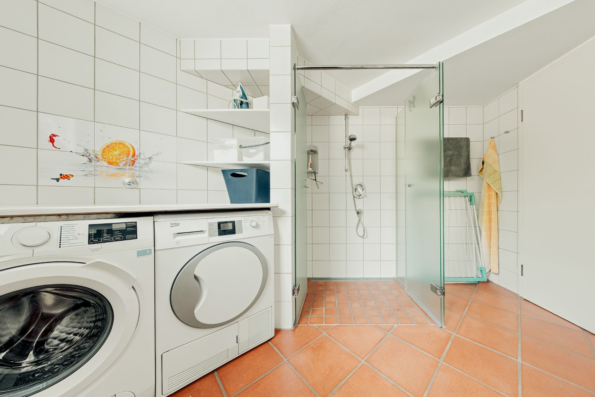 Modernes Bad mit Waschmaschine, Trockner, offener Dusche und weißen Fliesen.