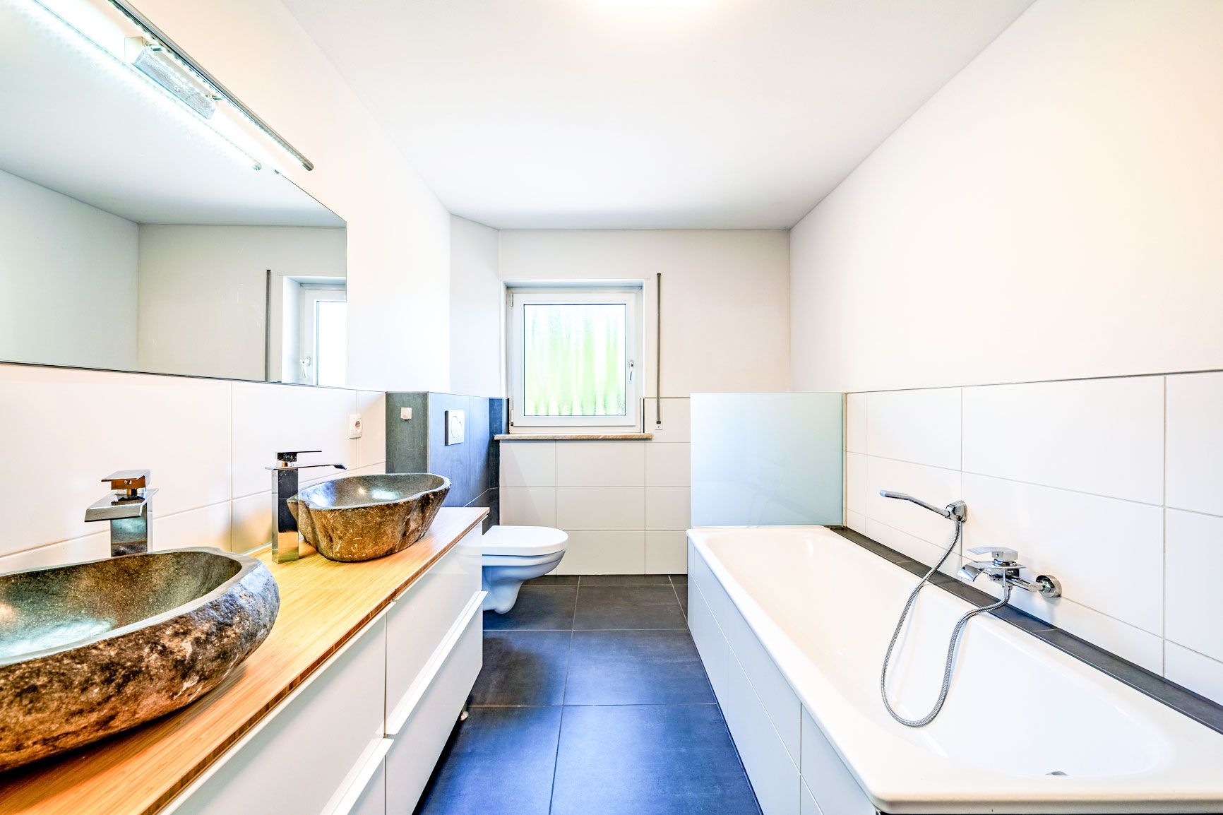 Modernes Badezimmer mit Badewanne, zwei Steinwaschbecken und großem Spiegel.