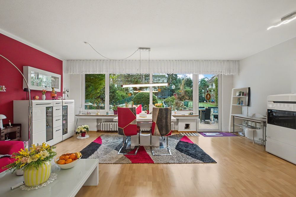 Helles Wohnzimmer mit Esstisch, bunzem Teppich und großen Fenstern mit Blick in den Garten.