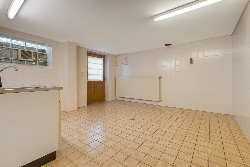Heller Raum mit Fliesenboden, Spülbecken, Heizkörper und Holztür mit Fenster.