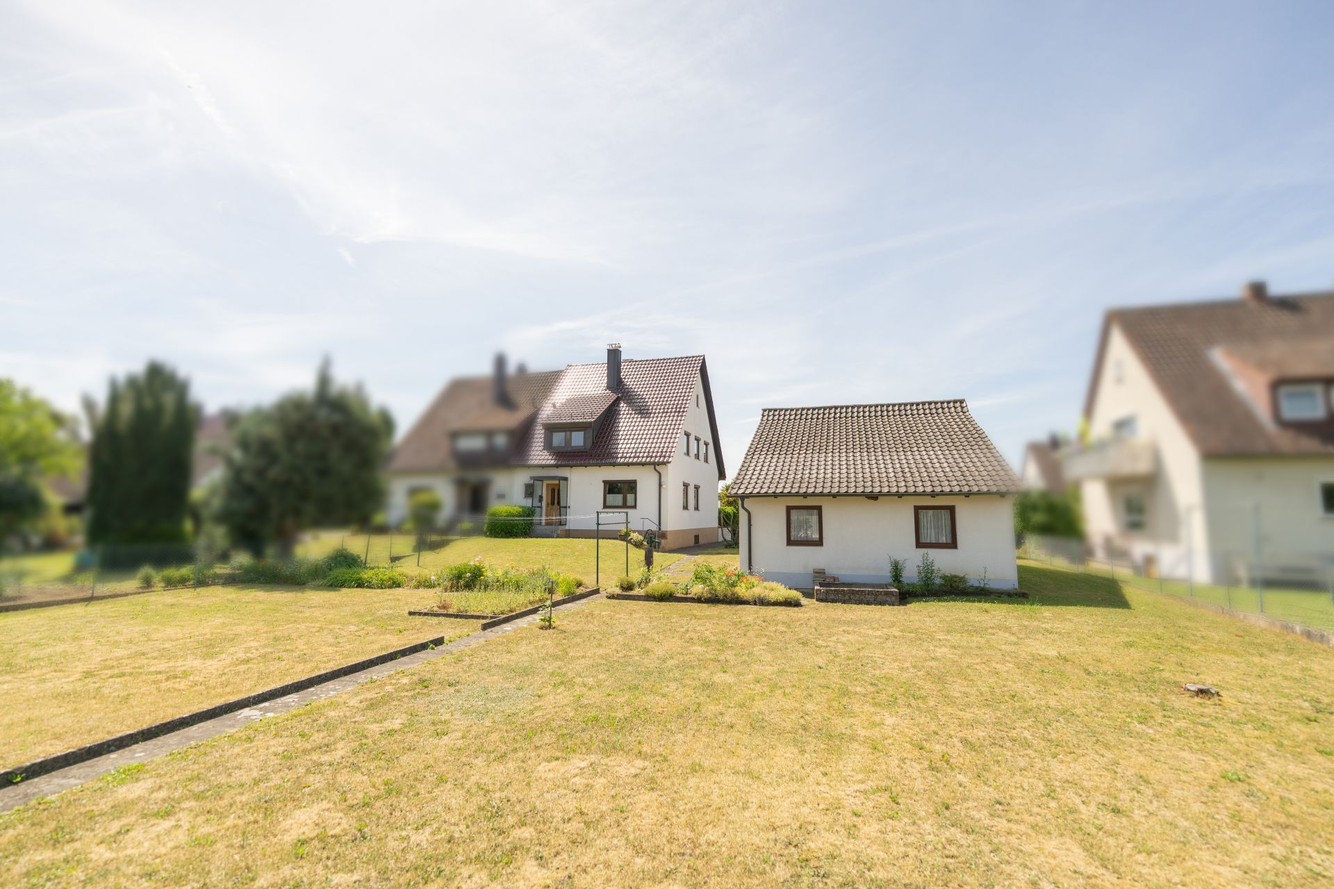 Zwei Einfamilienhäuser mit großem Garten bei sonnigem Wetter.