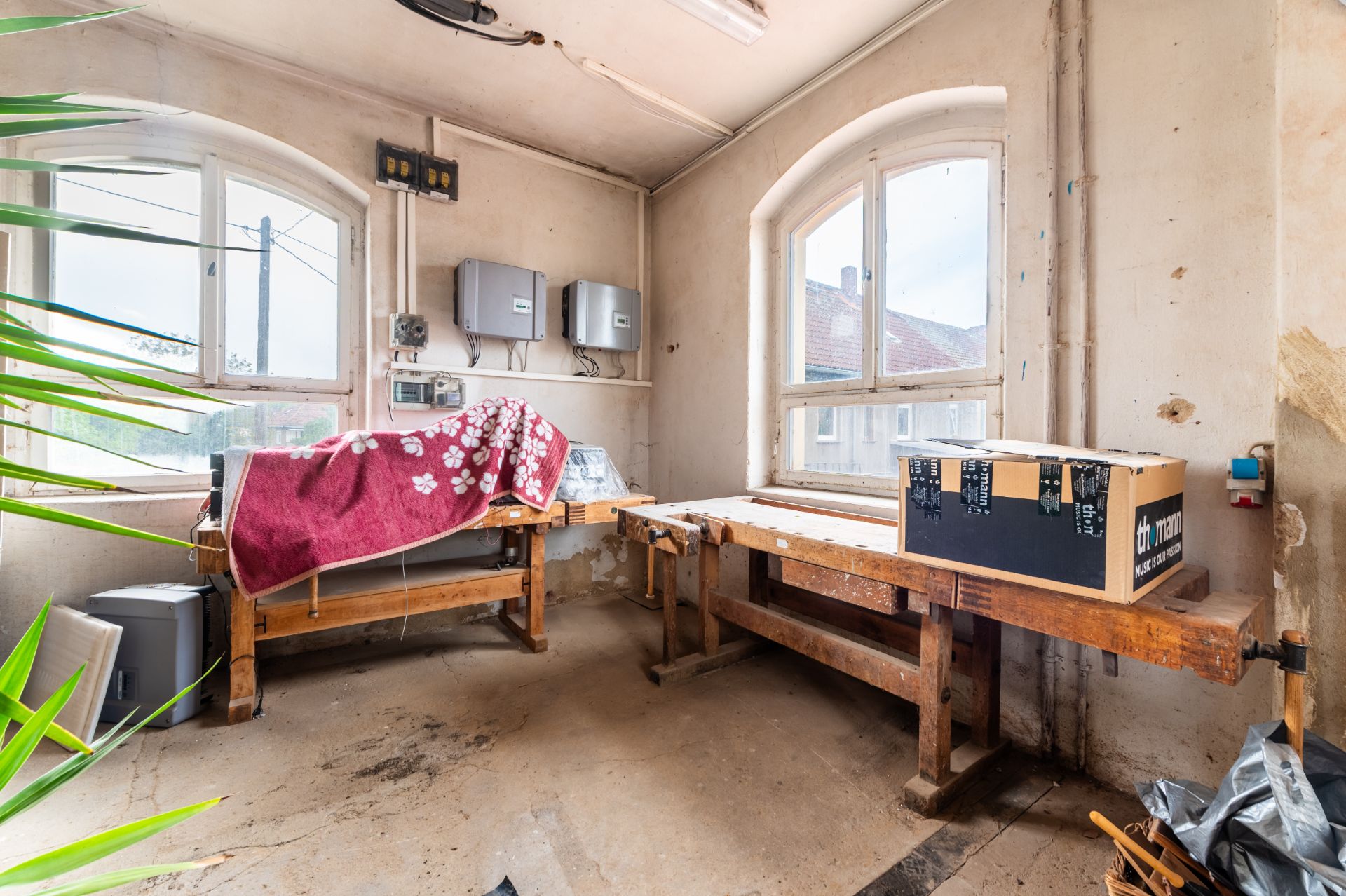 Heller Raum mit zwei Werkbänken, Karton, Fenster und technischen Geräten an der Wand.