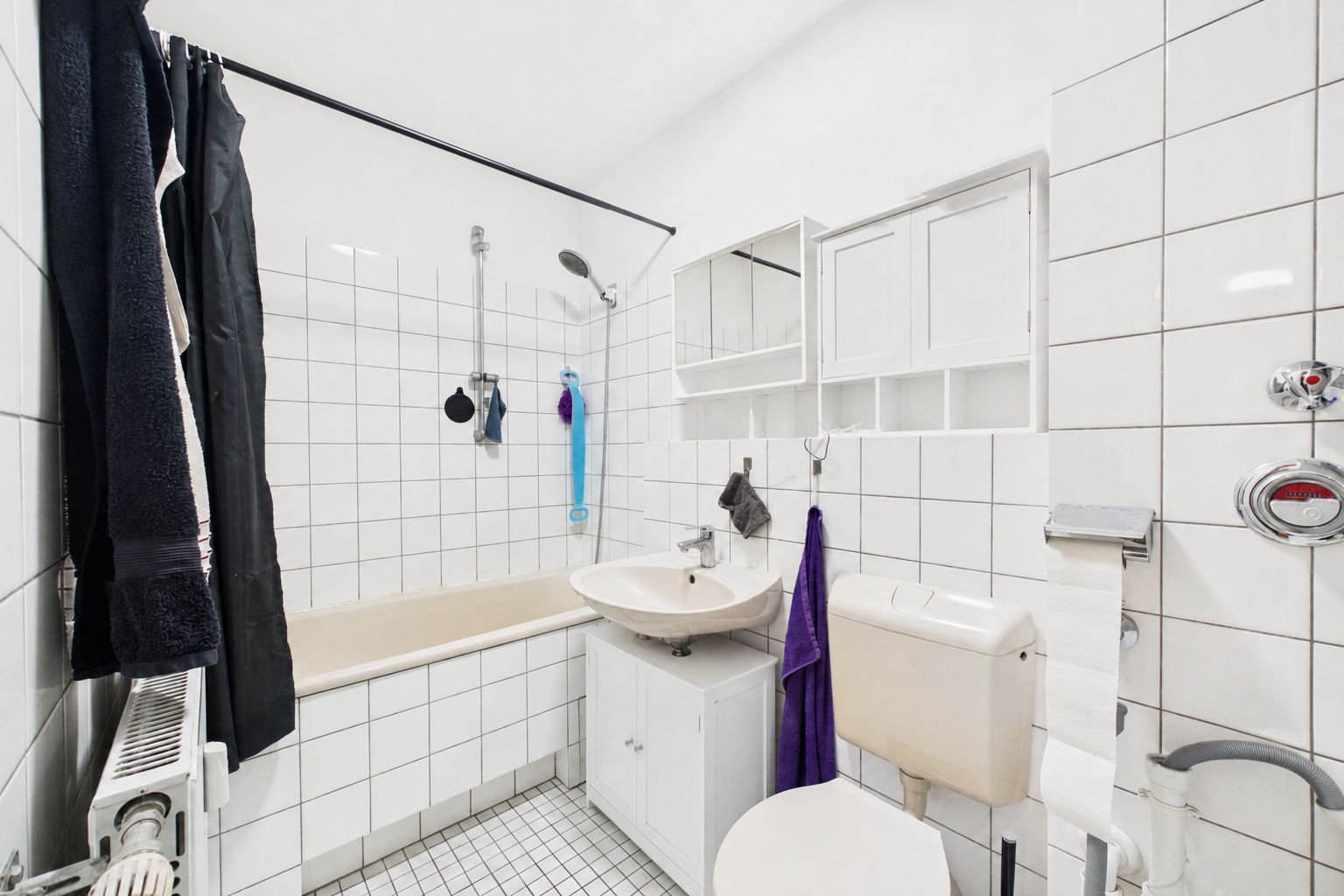 Helles Badezimmer mit Badewanne, Waschbecken, Toilette und weißen Fliesen.