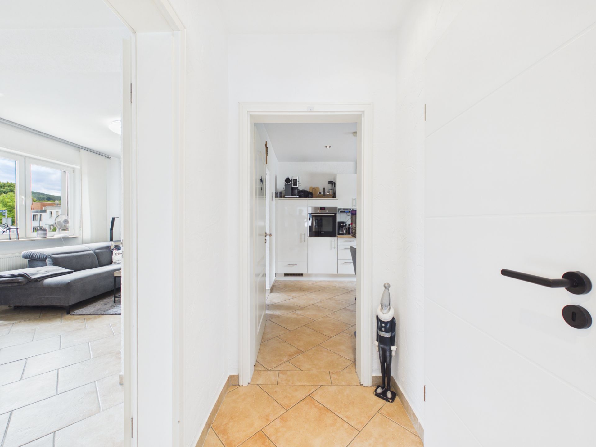Heller Flur mit Blick in die Küche und ins Wohnzimmer mit Sofa und großen Fenstern.