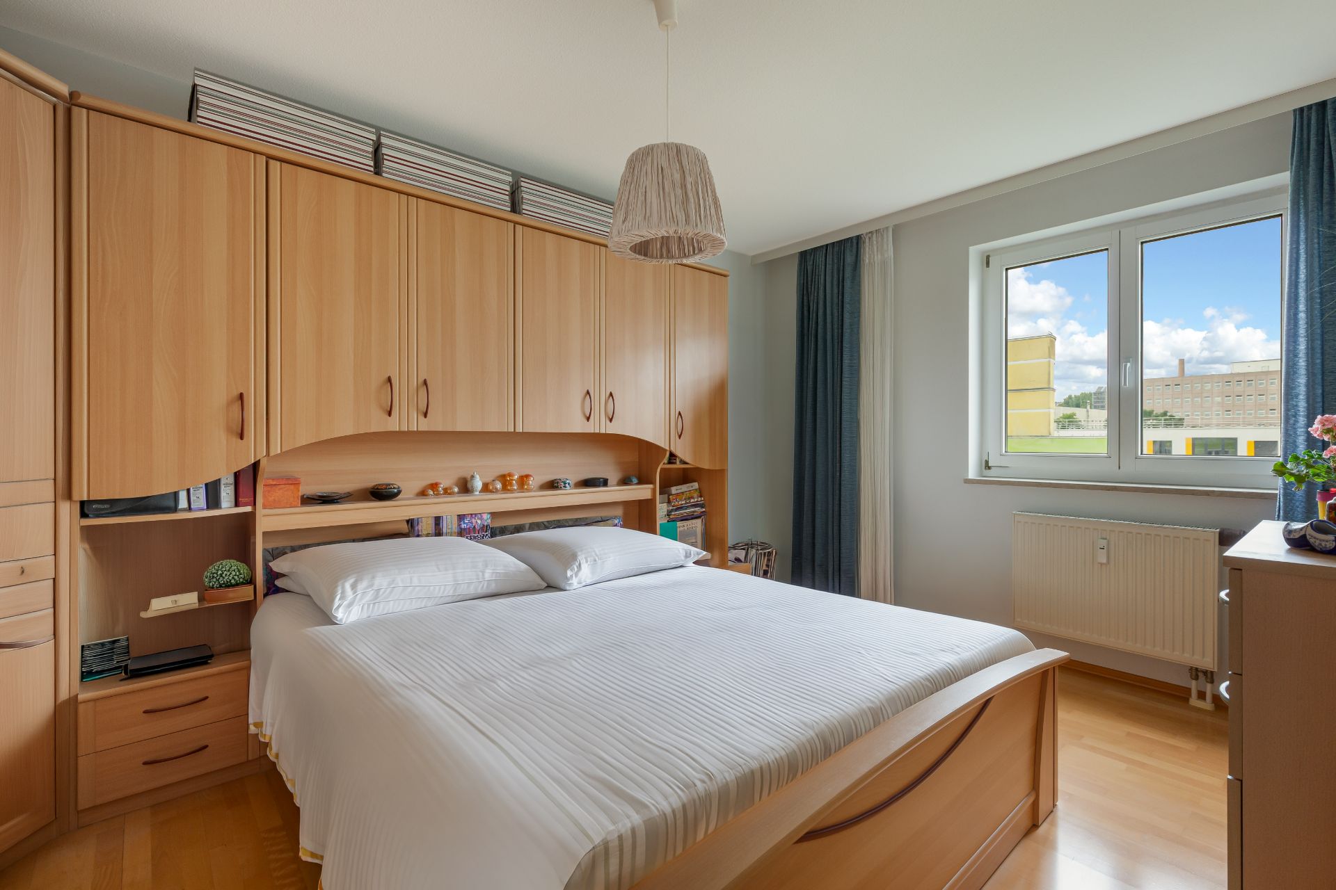 Schlafzimmer mit großem Bett, Holzschrankwand und Fenster mit Blick nach draußen.