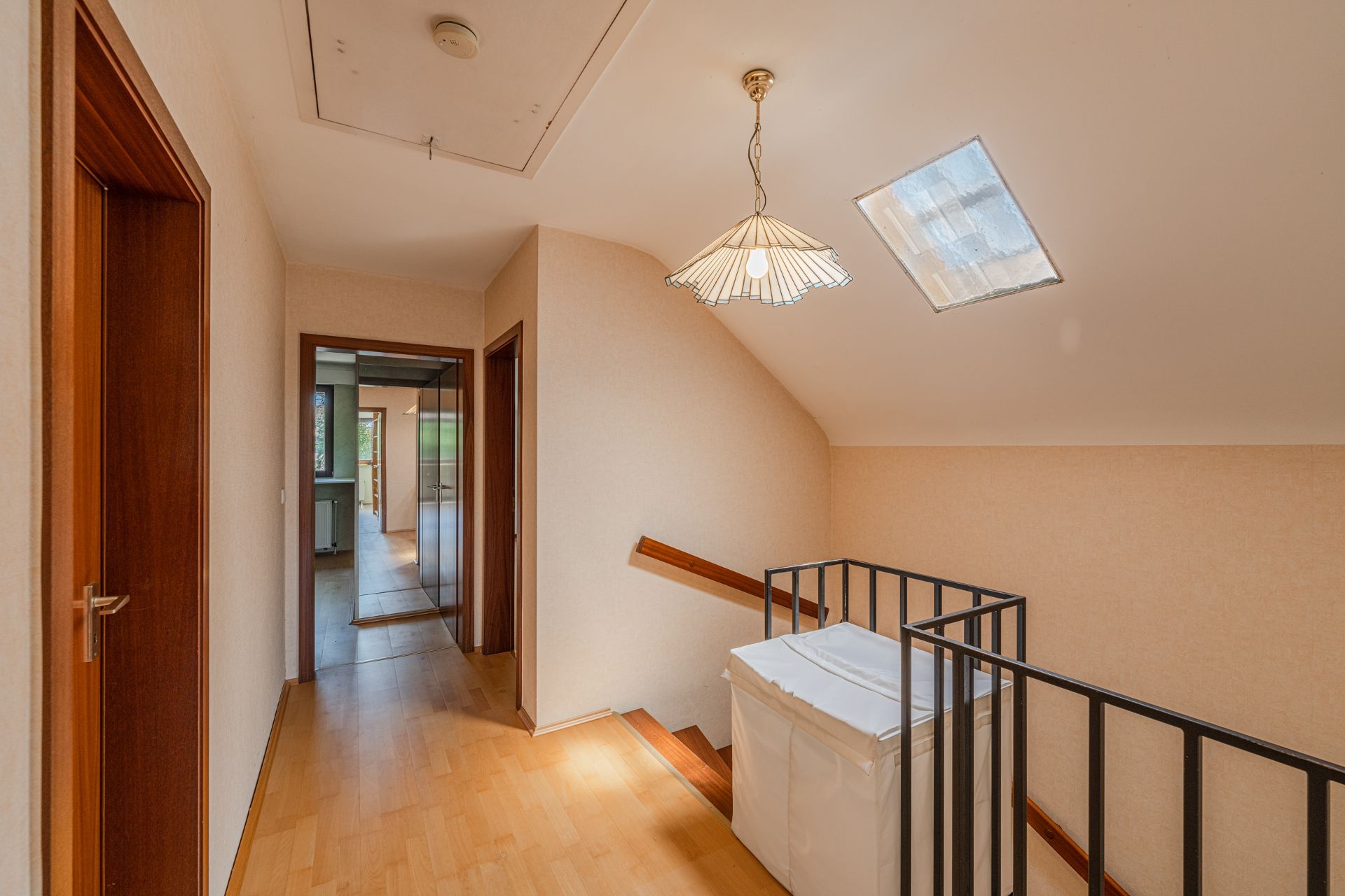 Heller Flur mit Holzfußboden, Treppengeländer und Hängeleuchte unter Dachfenster.