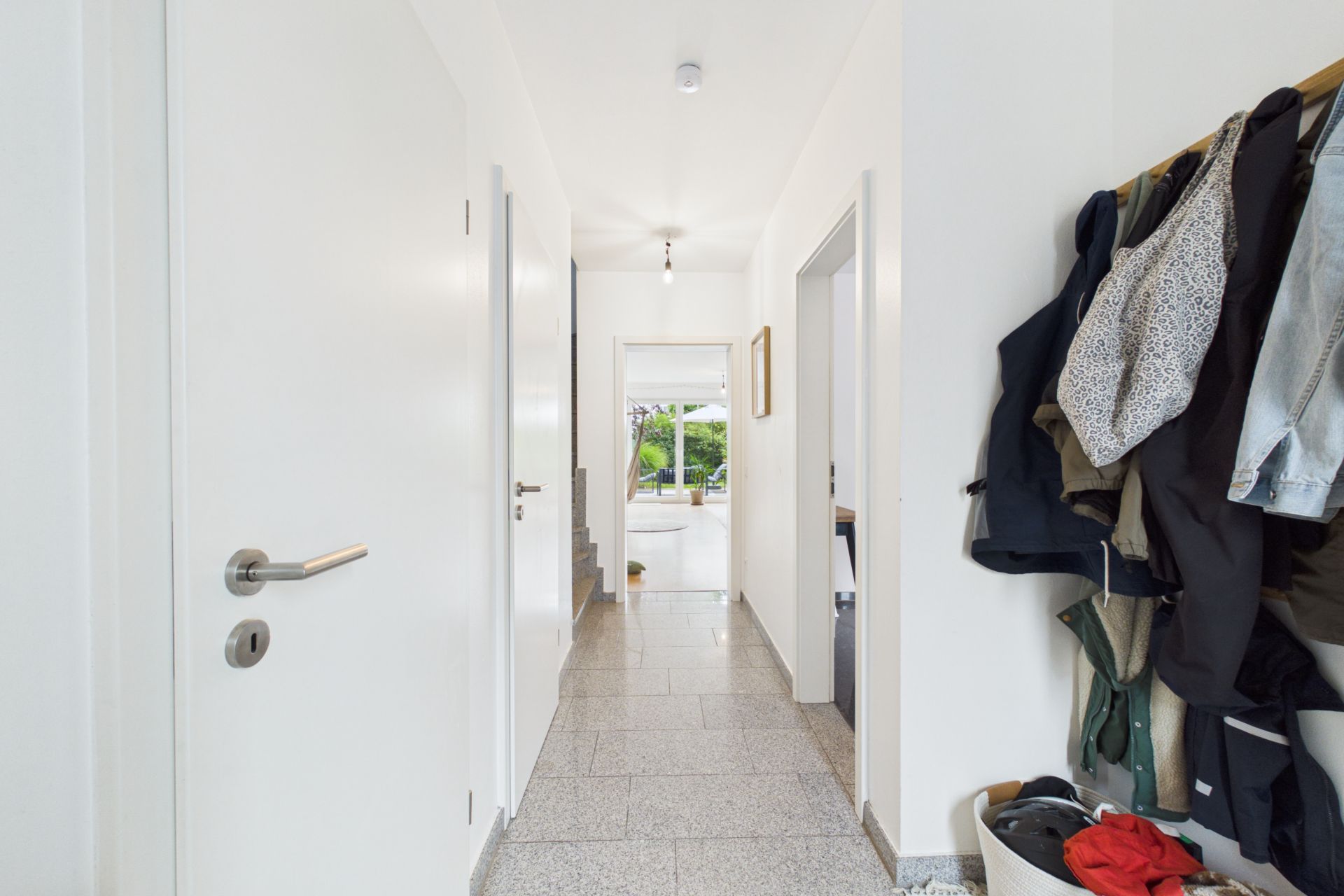 Heller Flur mit Garderobe und Blick in einen Raum mit großen Fenstern und Garten.