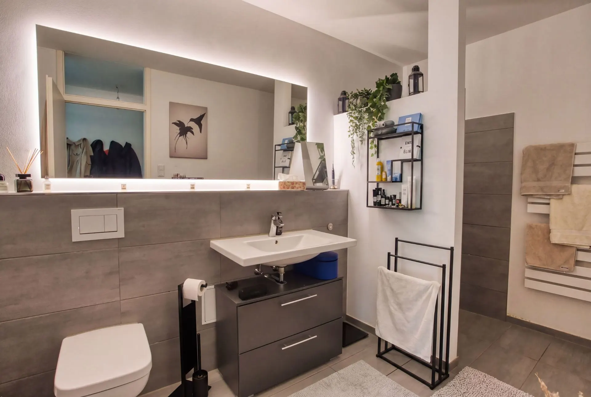 Modernes Badezimmer mit großem Spiegel, Waschbecken, Toilette und Handtuchhaltern.