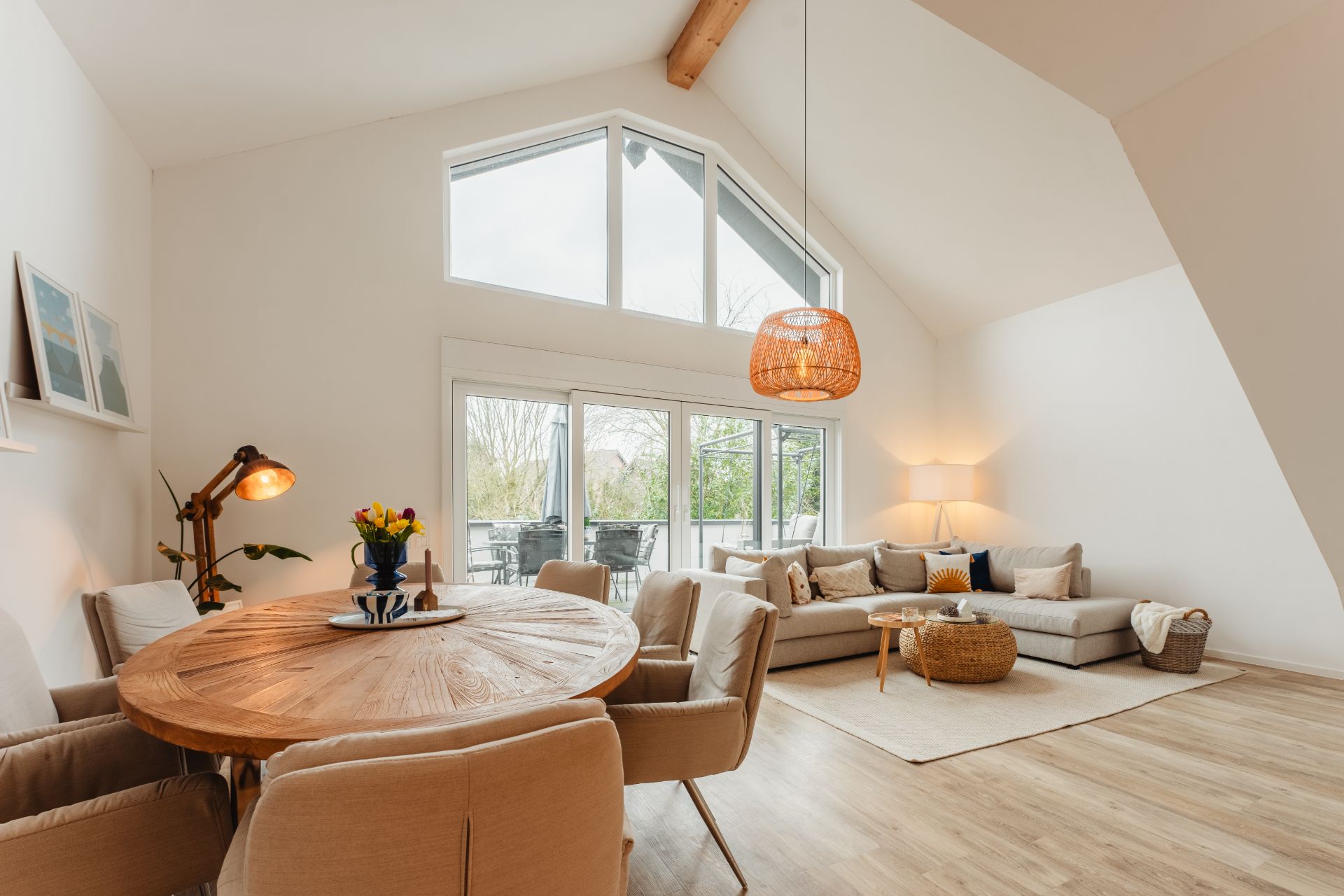 Helles Wohnzimmer mit großem Fenster, Ecksofa, rundem Esstisch und Holzfußboden.