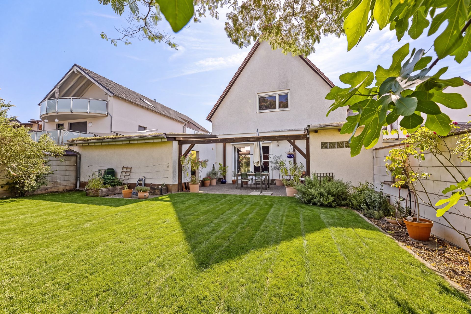 Gepflegter Garten mit Rasen, Terrasse und Einfamilienhaus im Hintergrund.