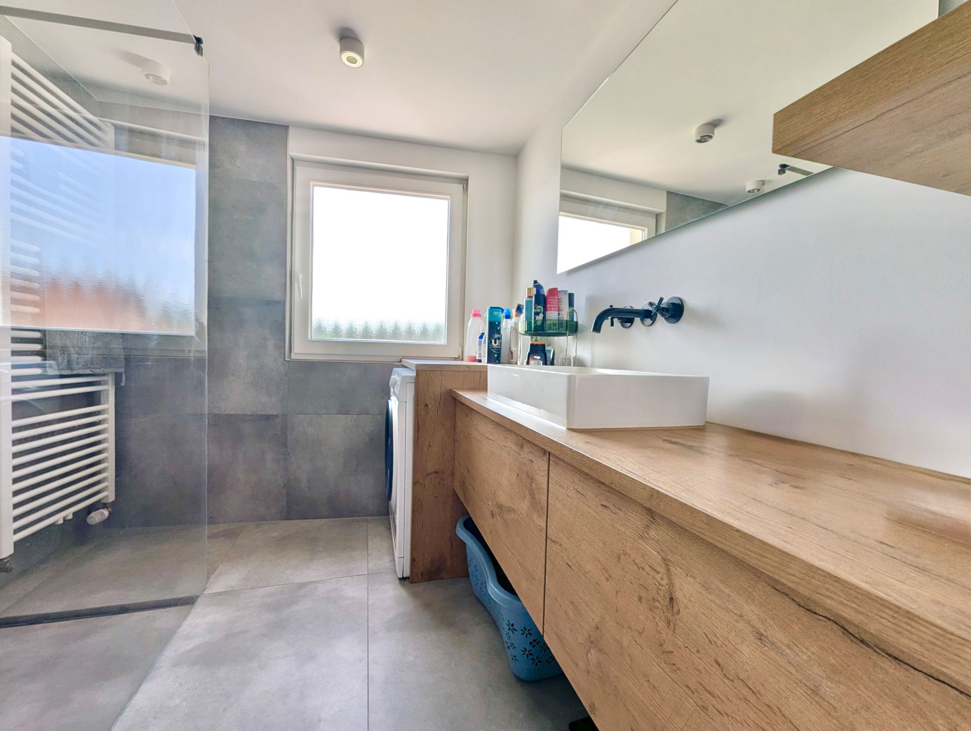 Modernes Badezimmer mit Holzwaschtisch, großem Spiegel, Dusche und Fenster.