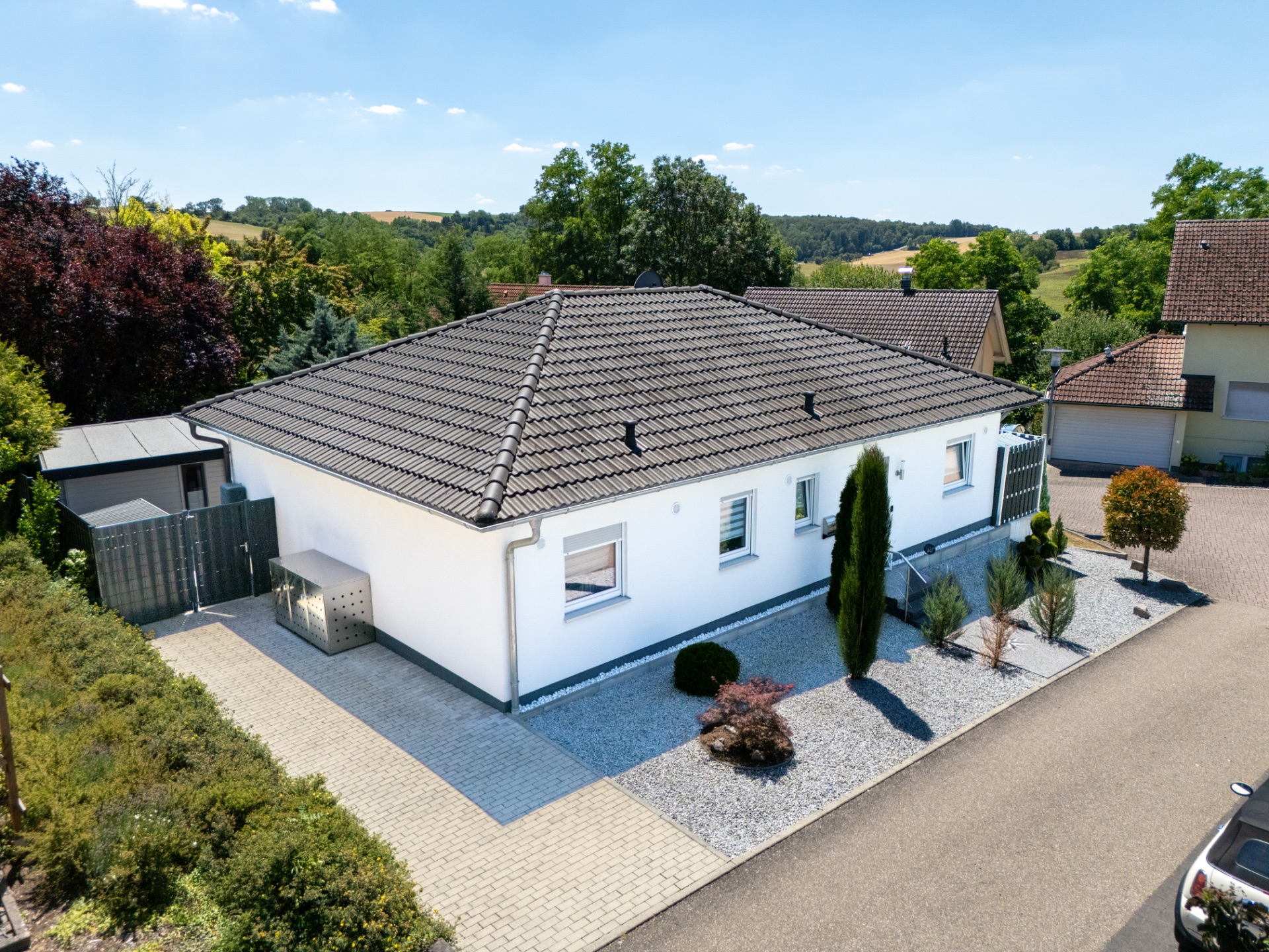 Weißes eingeschossiges Haus mit grauem Dach und gepflegtem Vorgarten an einer Straße.