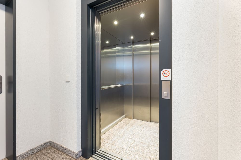 Geöffneter Aufzug mit Edelstahlwänden und beleuchtetem Innenraum in einem Wohngebäude.