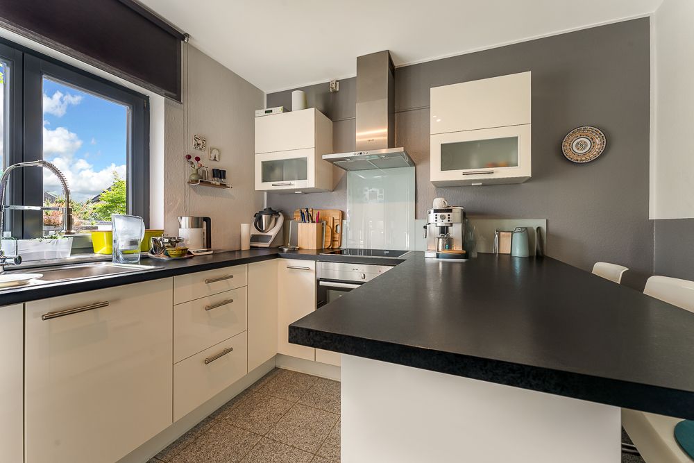 Moderne Küche mit weißen Schränken, schwarzer Arbeitsplatte und großen Fenstern.