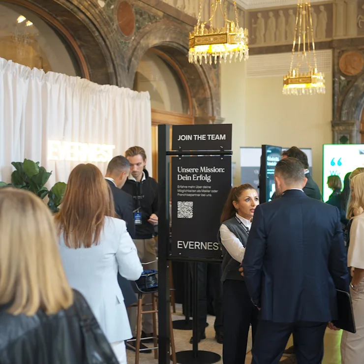 Mehrere Menschen im Gespräch in einem eleganten Foyer mit Marmorsäulen und Infotafeln.