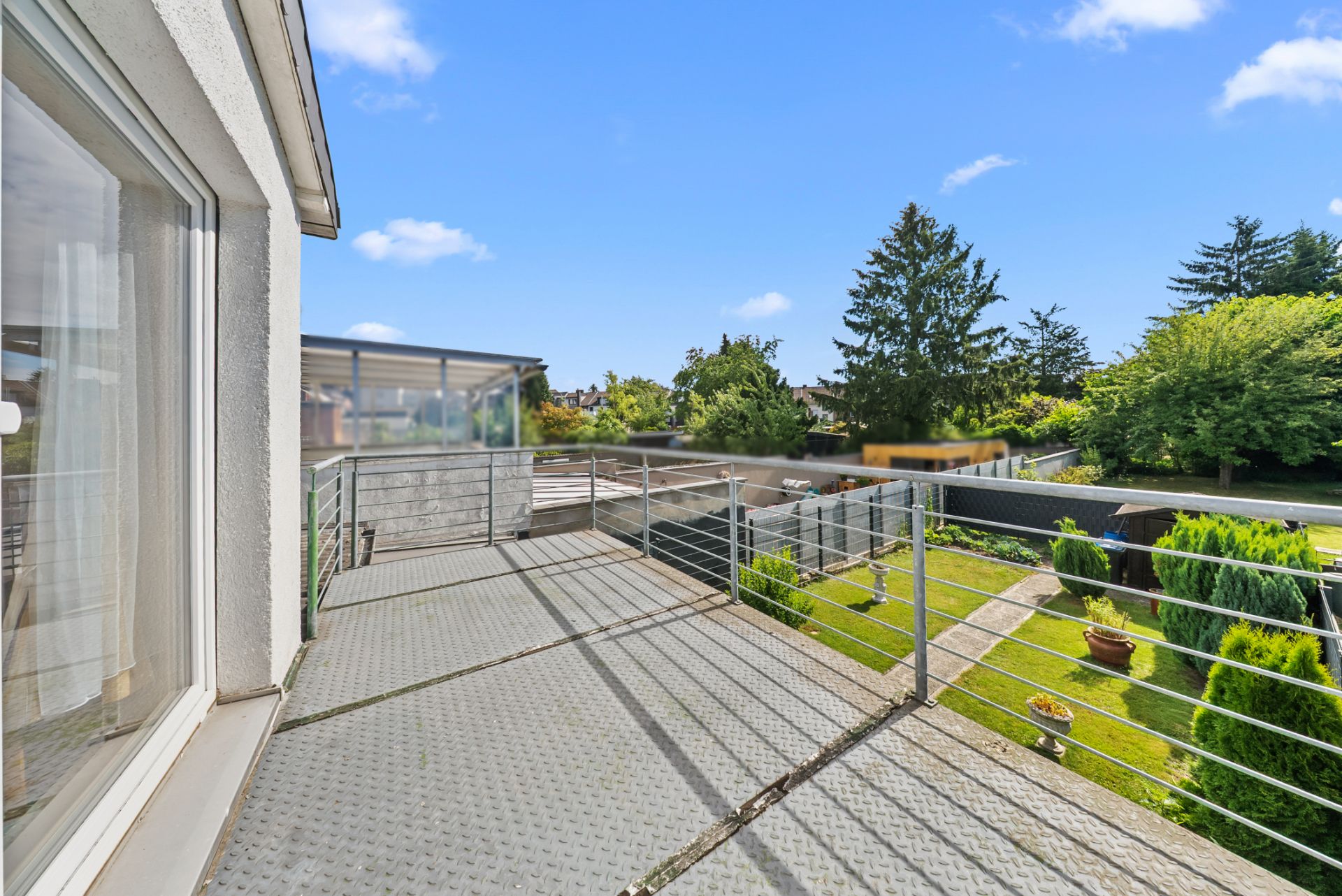 Offener Balkon mit Metallgeländer und Blick auf einen Garten mit Bäumen und Rasen.