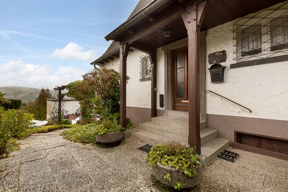Eingangsbereich eines Hauses mit überdachter Treppe und Pflanzenkübeln.