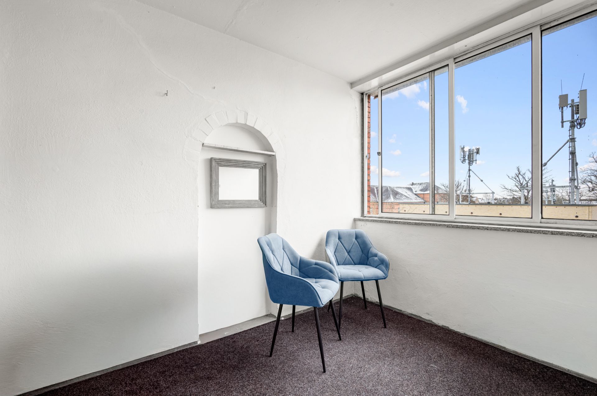 Heller Raum mit zwei blauen Stühlen an einem großen Fenster und weißer Wand.